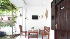 A patio with a wooden table and chairs, a potted plant, and a television mounted on the wall. - OYO 95108 Nareswari Homestay Syariah (Nogosari)