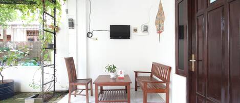 A patio with a wooden table and chairs, a potted plant, and a television mounted on the wall.