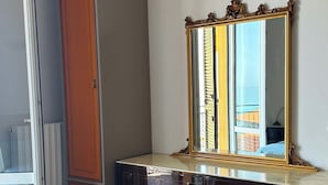 Een kamer met een houten garderobe, een donkere dressoir met lades, een grote spiegel en een lichtkleurig tapijt.
