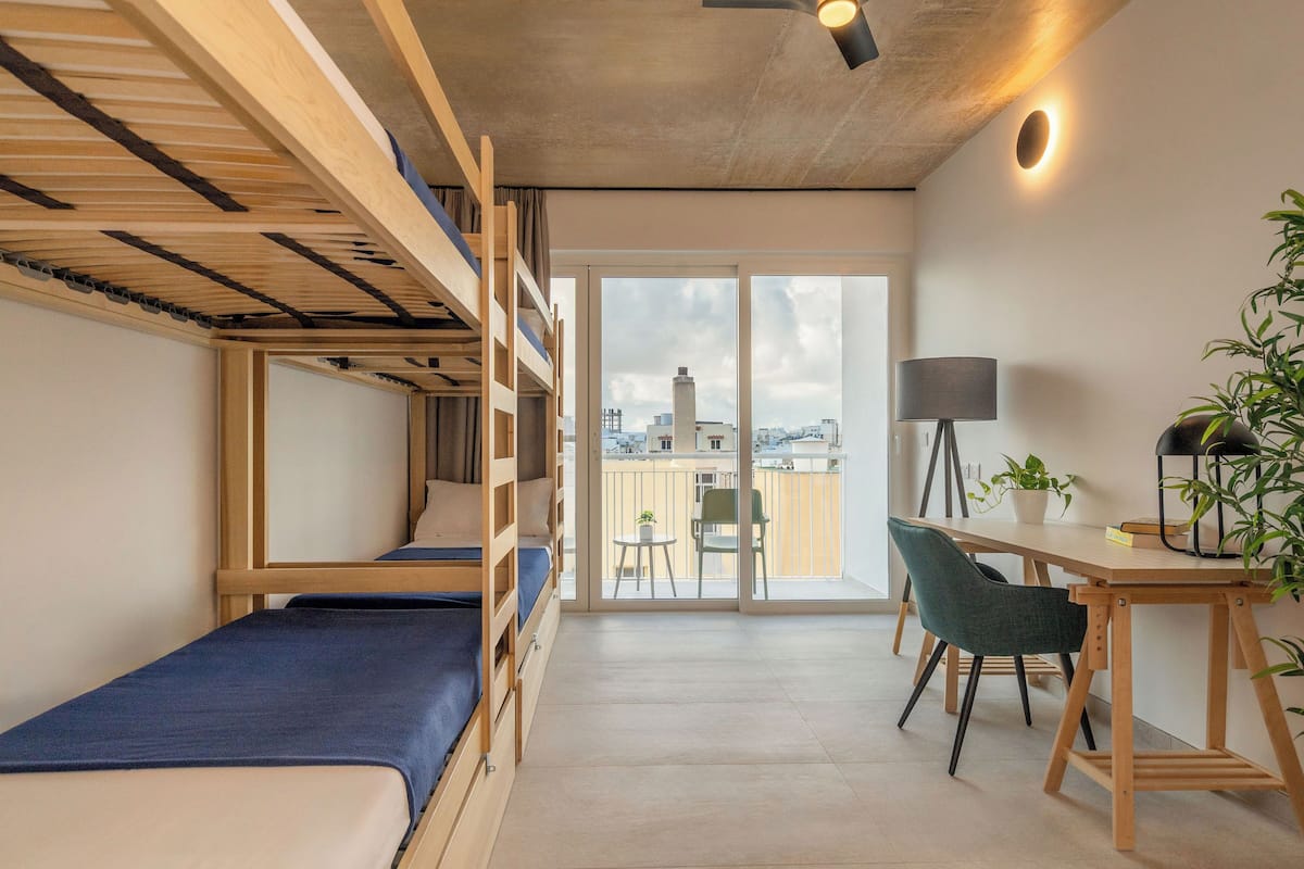 Une petite pièce comprenant des lits superposés, un bureau, une chaise, une lampe et une plante en pot.