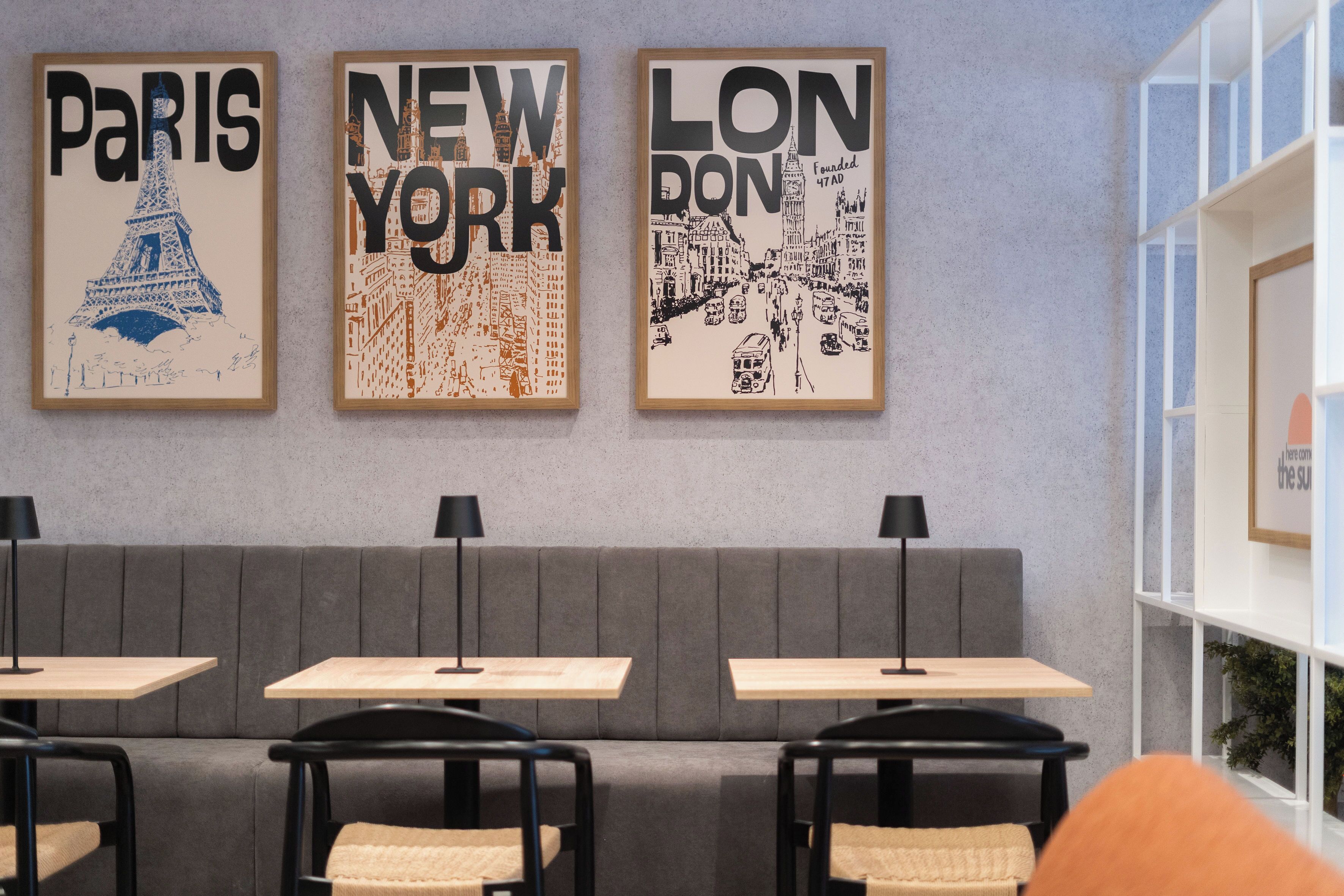A modern interior with a grey sofa, three framed city posters, and minimalist tables and chairs.