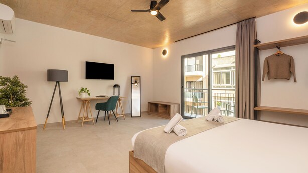 Moderni hotellihuone, jossa on suuri sänky, työpöytä tuolilla, televisio ja parveke, jolta on näkymä.