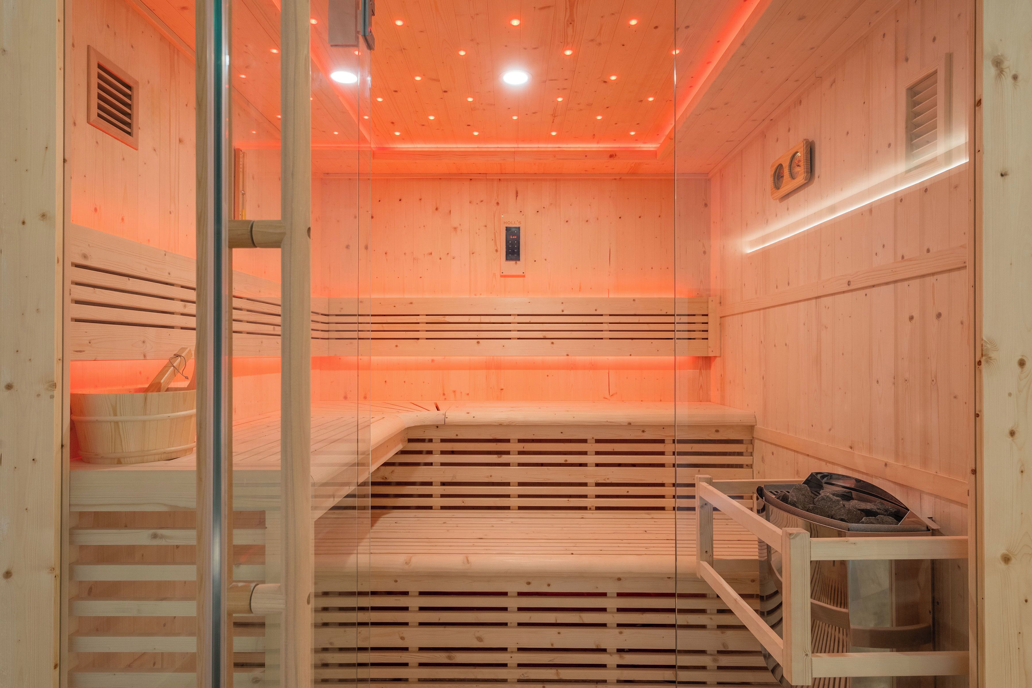 Una sauna con paredes y bancos de madera, una puerta de cristal y un panel de control en la pared.