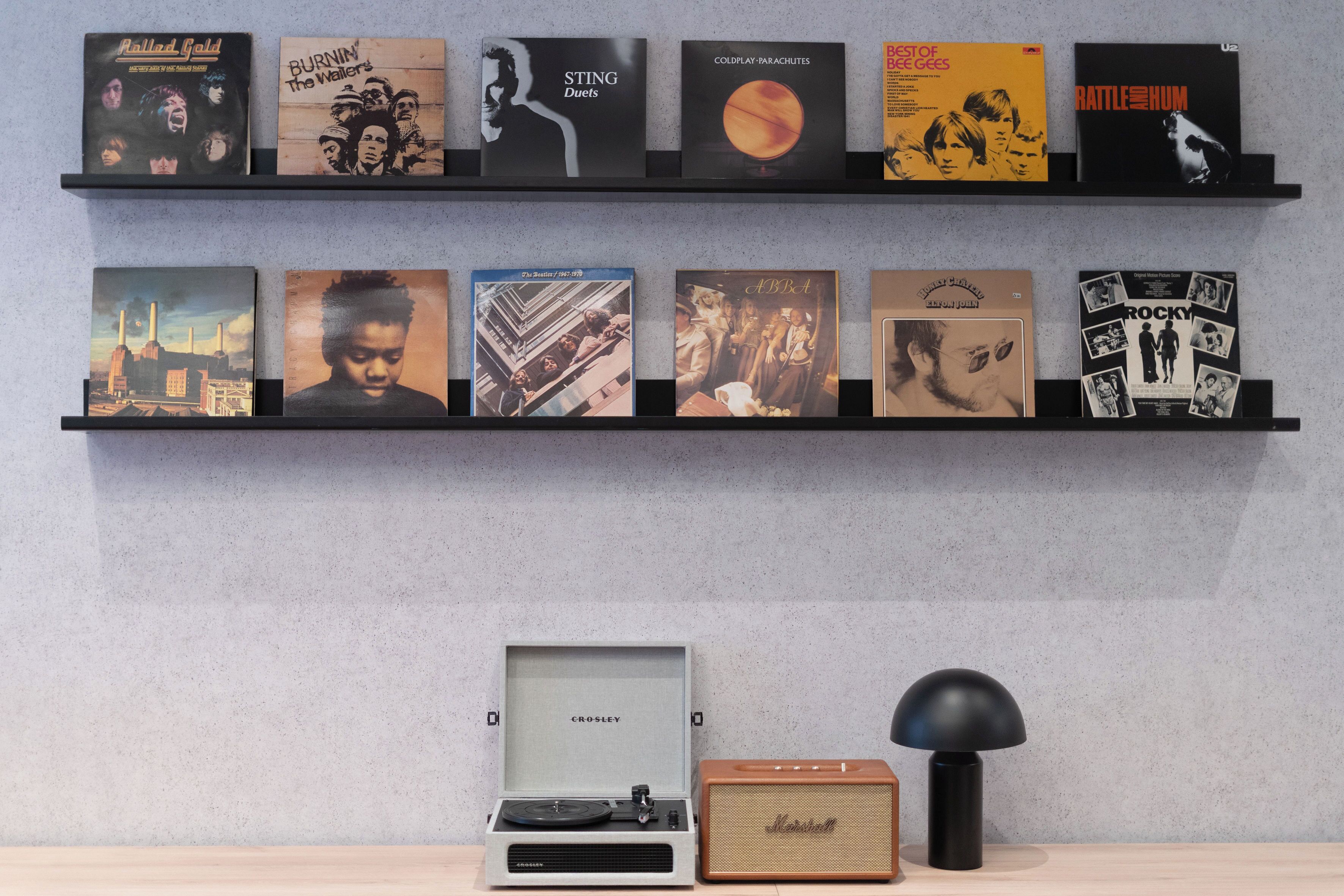 En samling vinylplader på to hylder foran en ensfarvet væg.