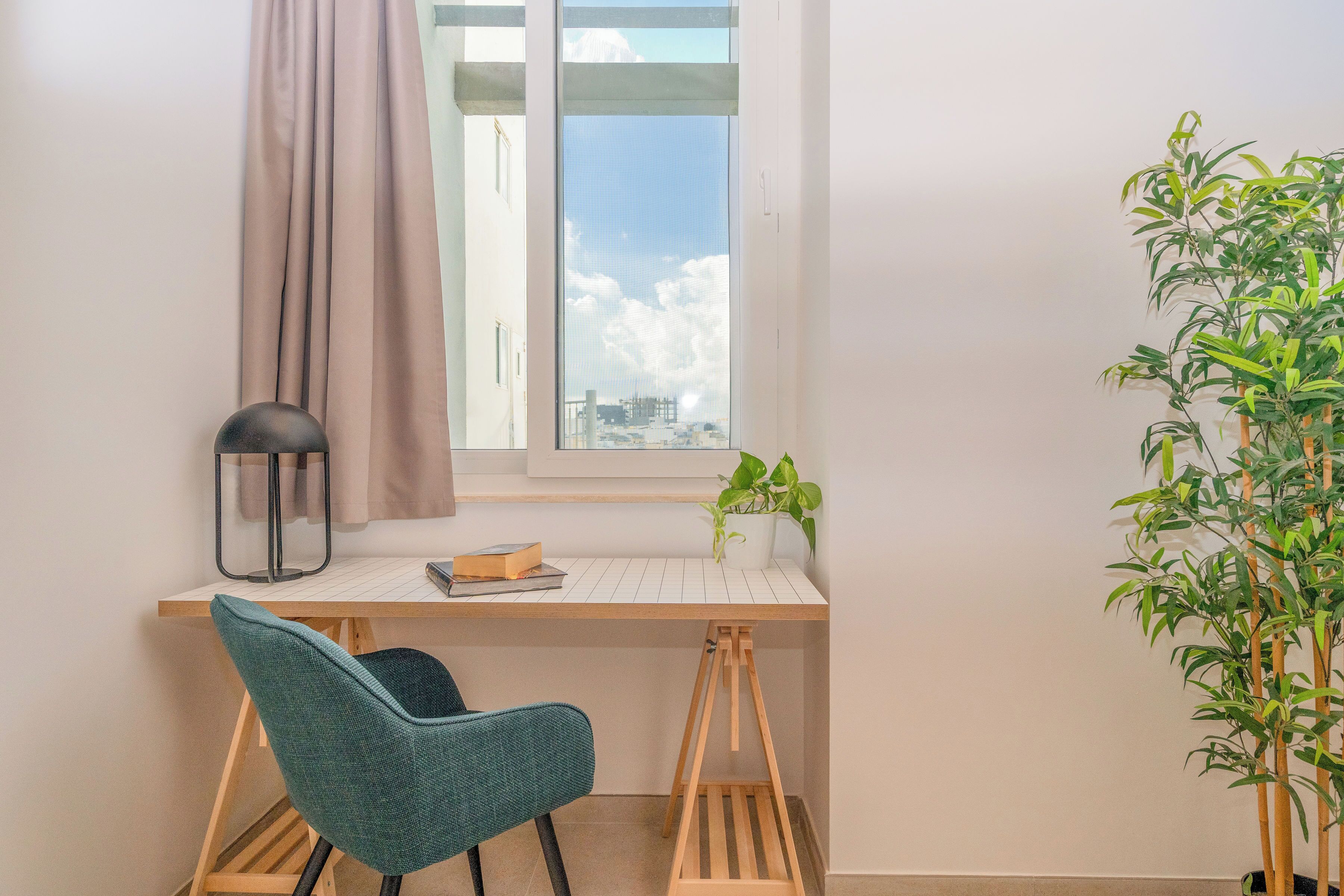 Un espacio de trabajo con escritorio, silla, ventana, cortina y una planta en maceta.