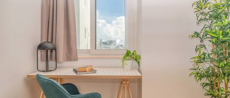 A workspace with a desk, chair, window, curtain, and a potted plant.