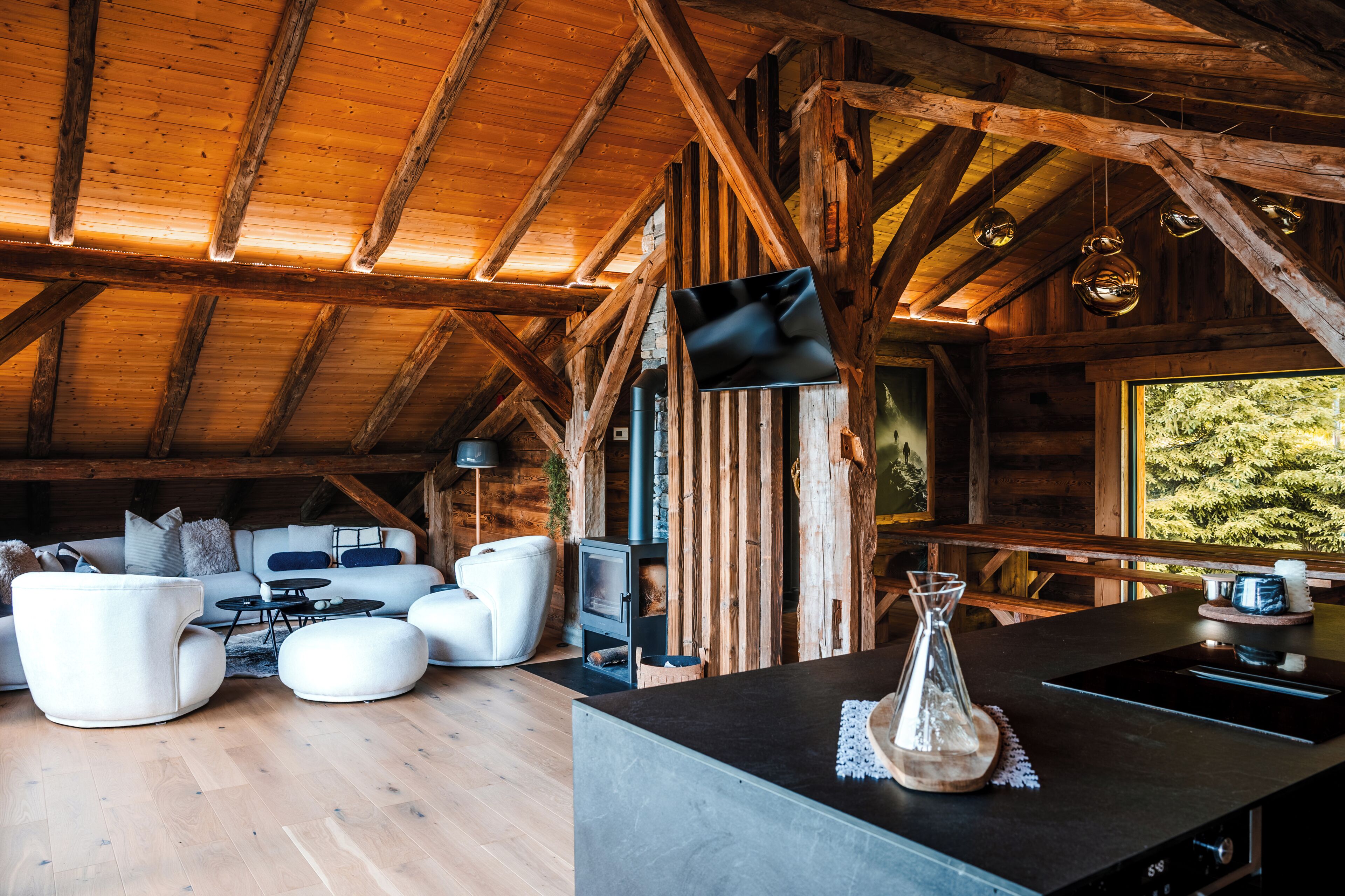A rustic wooden cabin interior with a sofa set, a fireplace, and a kitchen area.