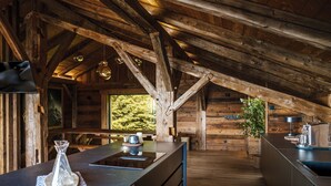 Interno rustico di una baita di legno con angolo cottura dotato di un'isola grande, travi in legno e vista sull'esterno.