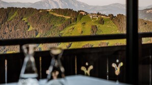 Vista dalla finestra con un tavolo in primo piano, che mostra un paesaggio con montagne e una zona boschiva.