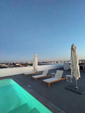 A rooftop pool area with lounge chairs and umbrellas, overlooking a cityscape. - 2-bedroom apartment in charming West Hollywood with AC and gym access (West Hollywood)