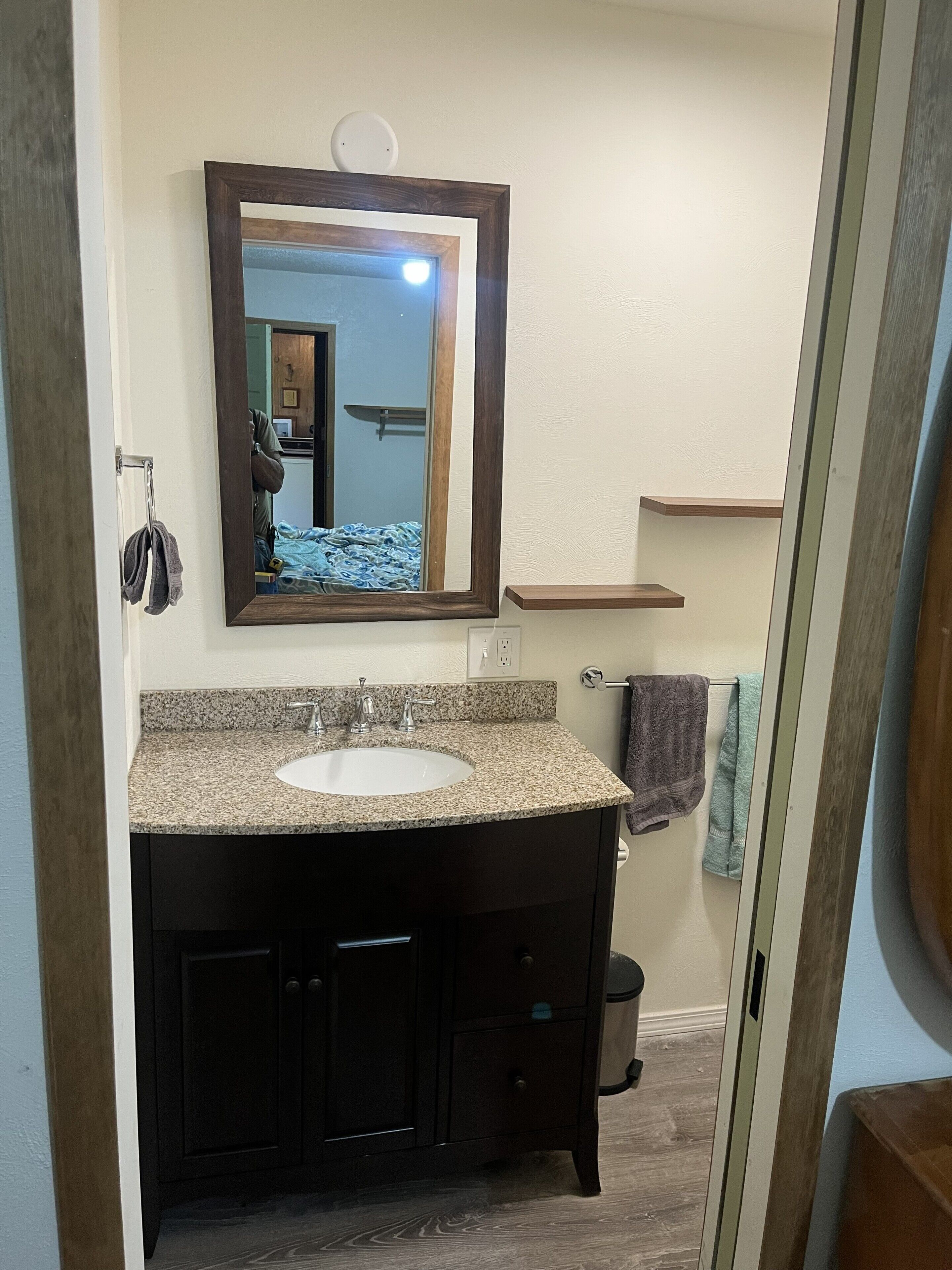 Un bagno con lavabo su piano in granito, mobili in legno scuro, uno specchio grande e un porta asciugamani.