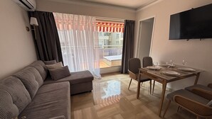 A modern living room with a sofa, dining table, chairs, and a TV. - Apartment Terrace Next to the Sea (Nice)