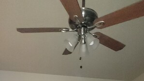 Un dormitorio con cama de madera, ventilador de techo, dos mesitas de noche con lámparas y un cuadro colgado en la pared.