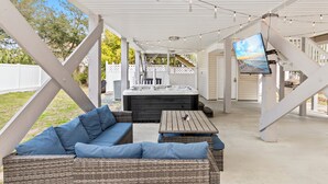 An outdoor covered patio with a hot tub, wicker furniture, and a TV screen. - Private Heated Pool, Hot Tub, 1-min Walk to Beach, Pet Friendly, King Bed (Surfside Beach)