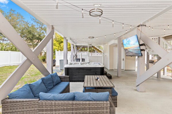 An outdoor covered patio with a hot tub, wicker furniture, and a TV screen. - Private Heated Pool, Hot Tub, 1-min Walk to Beach, Pet Friendly, King Bed (Surfside Beach)