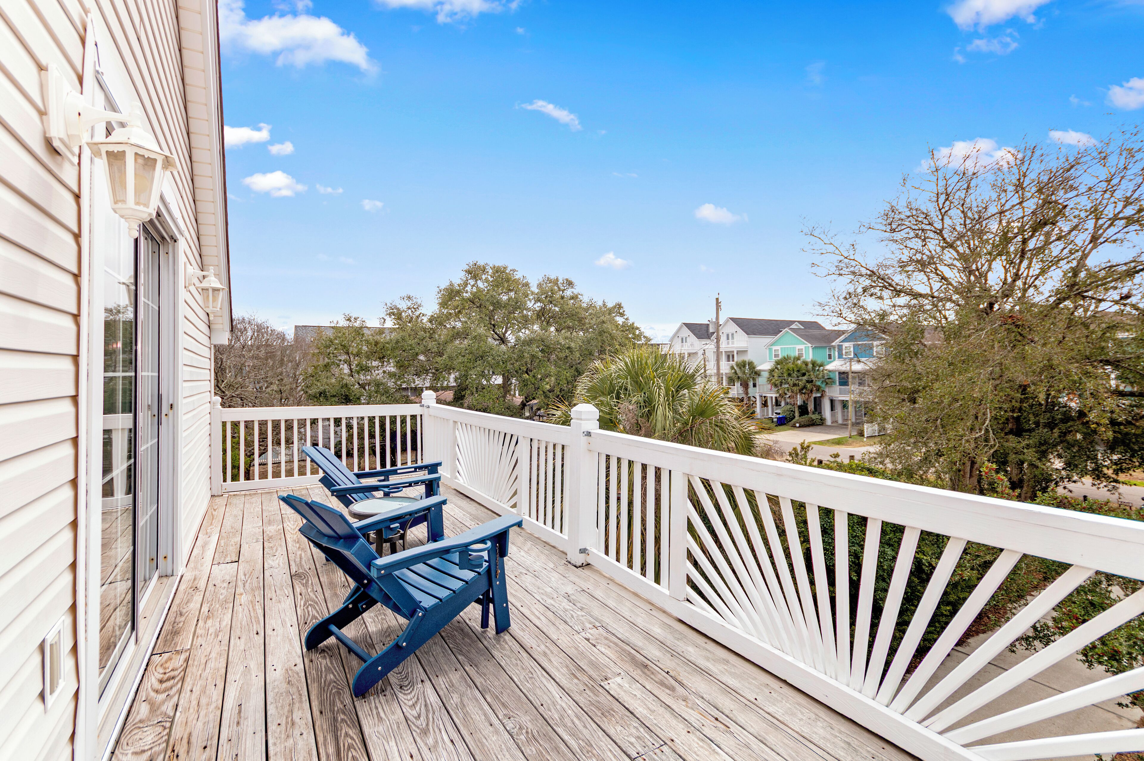 A wooden deck with a white railing, two blue Adirondack chairs, and a table.