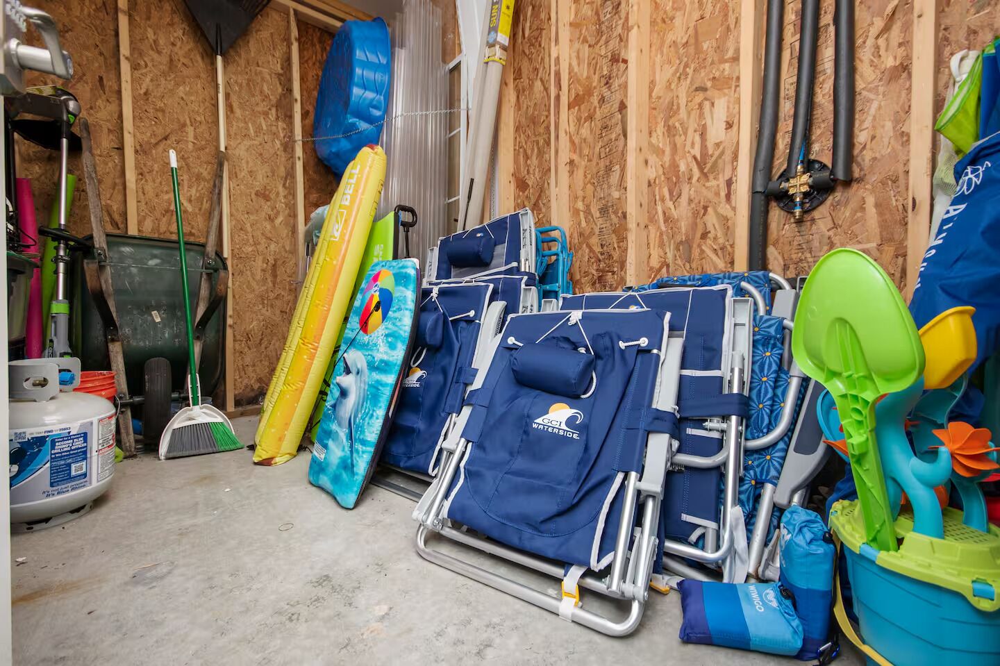Een opbergruimte met diverse spullen, waaronder een blauwe strandstoel, een opblaasbaar zwembad in geel en een groene luchtbed voor in het zwembad.
