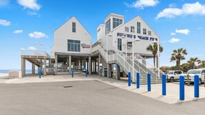 A beachfront building with a sign reading "Sunshine Beach Pit." It features a staircase leading to the entrance, a covered area, and a view of the beach. - Private Heated Pool, Hot Tub, 1-min Walk to Beach, Pet Friendly, King Bed (Surfside Beach)