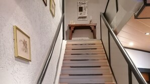 A staircase with wooden steps and a metal railing, leading to a landing with a small table and a welcome sign.