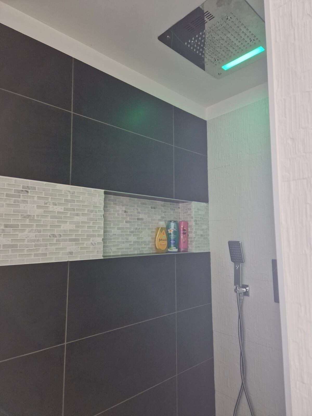 Ein Duschbereich mit schwarz-weißen Fliesen, Ablagefläche für Toilettenartikel und einer Handbrause.