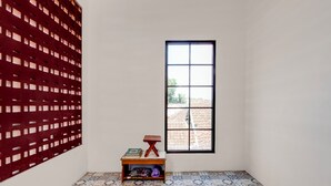 Une pièce avec un sol carrelé, une fenêtre donnant sur un beau paysage, une petite table en bois sur laquelle sont posés des livres, et un panneau décoratif rouge.