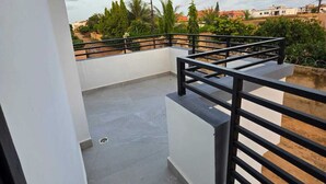 Une terrasse sur le toit, dotée d’une rambarde noire, d’un sol en béton et offrant une vue sur les bâtiments environnants et la végétation.