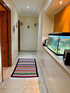 A hallway with a fish tank, a striped rug, and a wooden door. - La Baïa: Cozy (La soukra)