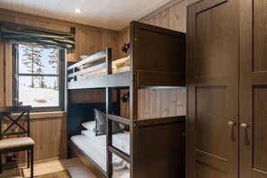 A bunk bed room with a window, a desk, and a wardrobe.