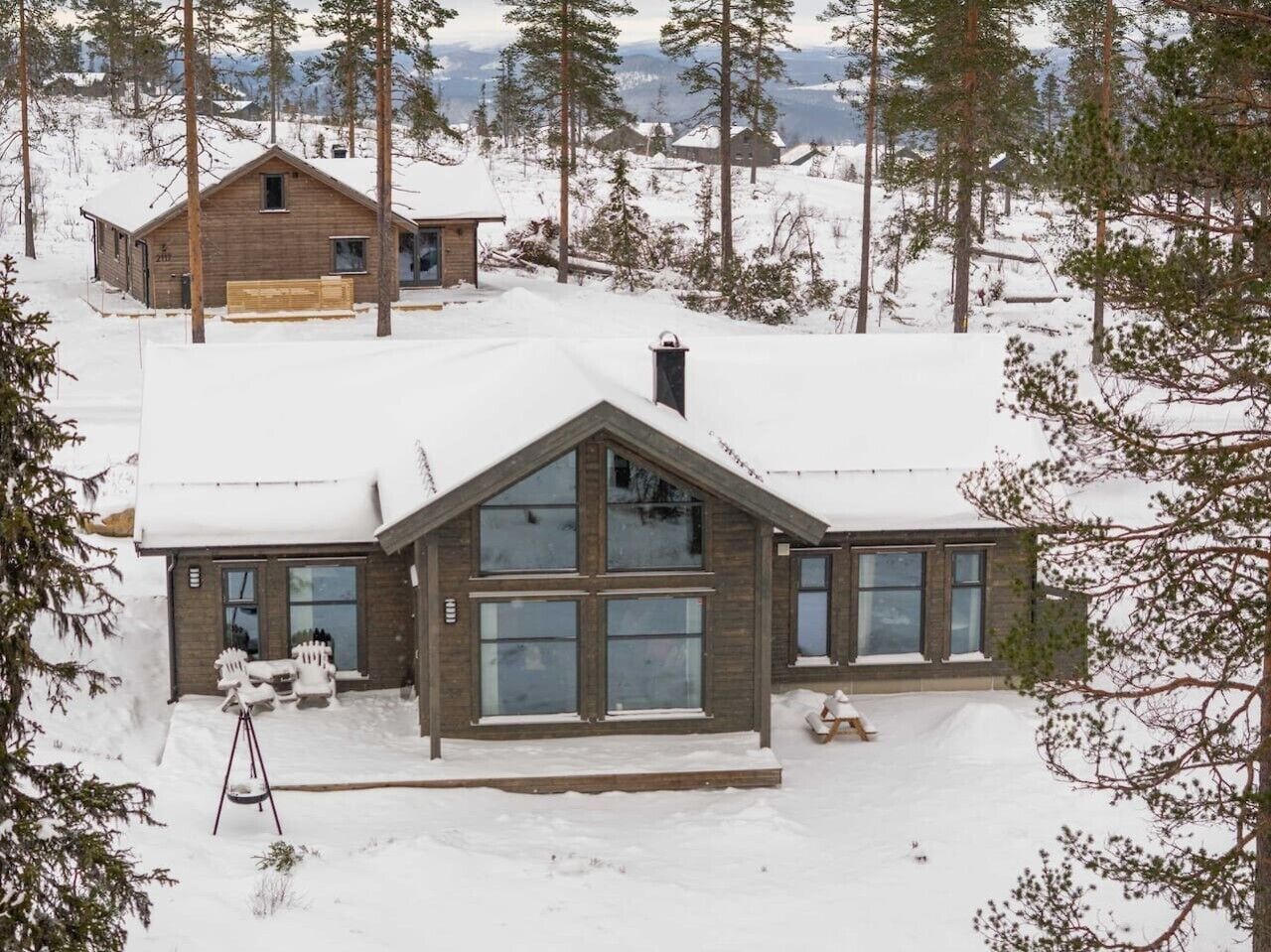Une cabane en bois dotée de grandes fenêtres, entourée d’arbres couverts de neige.