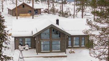 A wooden cabin with large windows, surrounded by snow-covered trees.