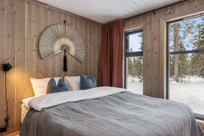 A bedroom with a bed, a wall fan, a window with curtains, and a view of trees.