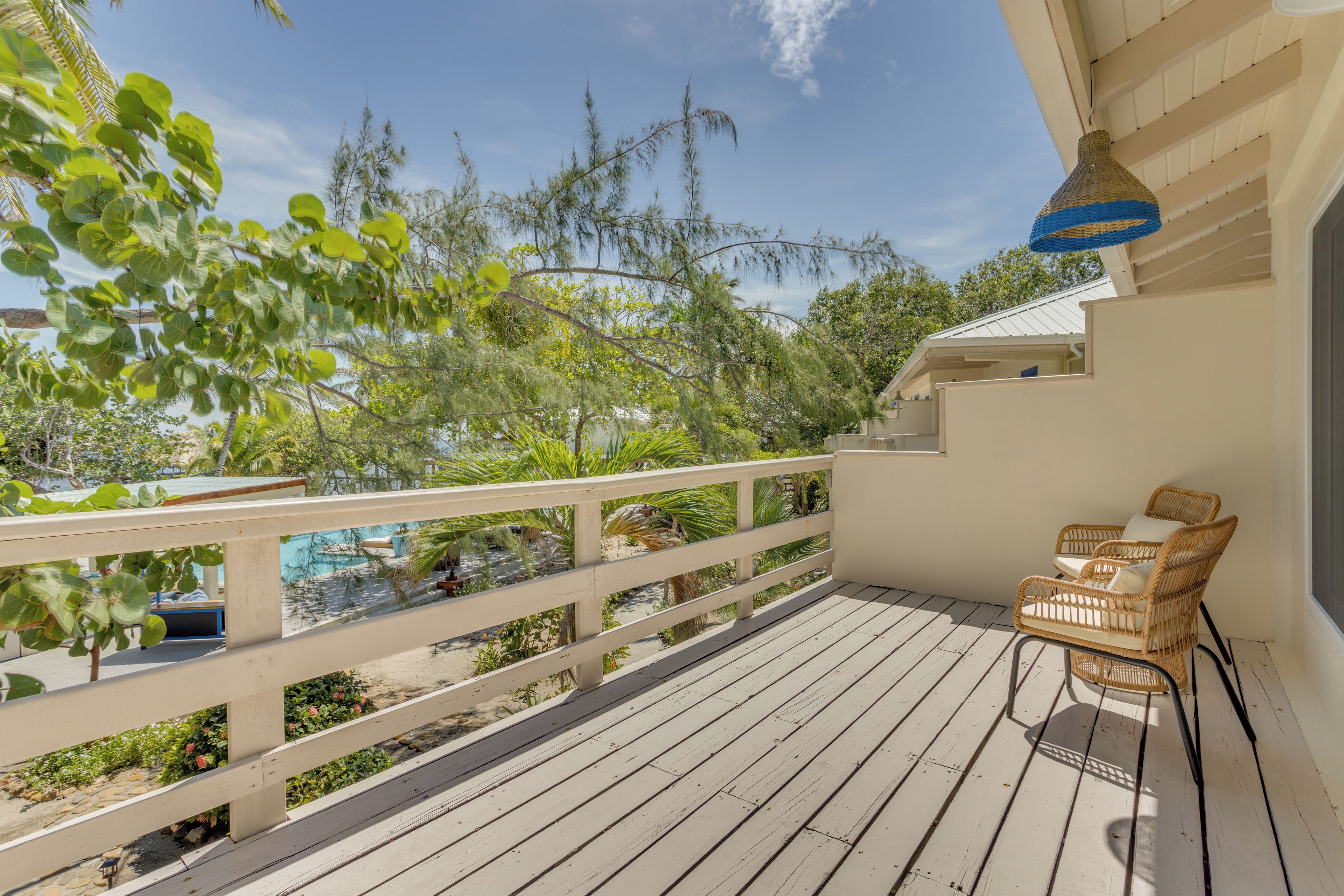 Une terrasse en bois, meublée de meubles en osier et agrémentée d’un luminaire suspendu.