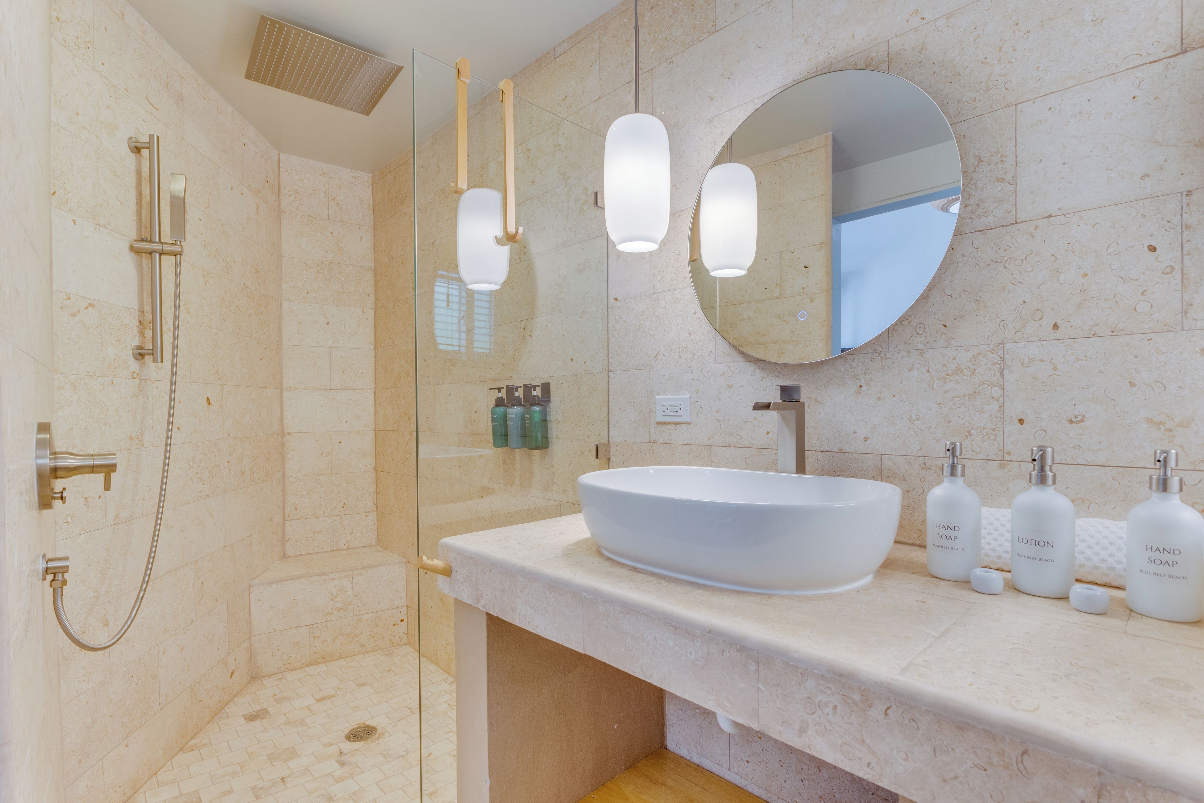 A modern bathroom with a large oval sink, a round mirror, and a glass-enclosed shower area.