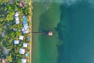 Vista aérea de un resort con varias cabañas, un mar turquesa cristalino y un muelle que se adentra en el agua.
