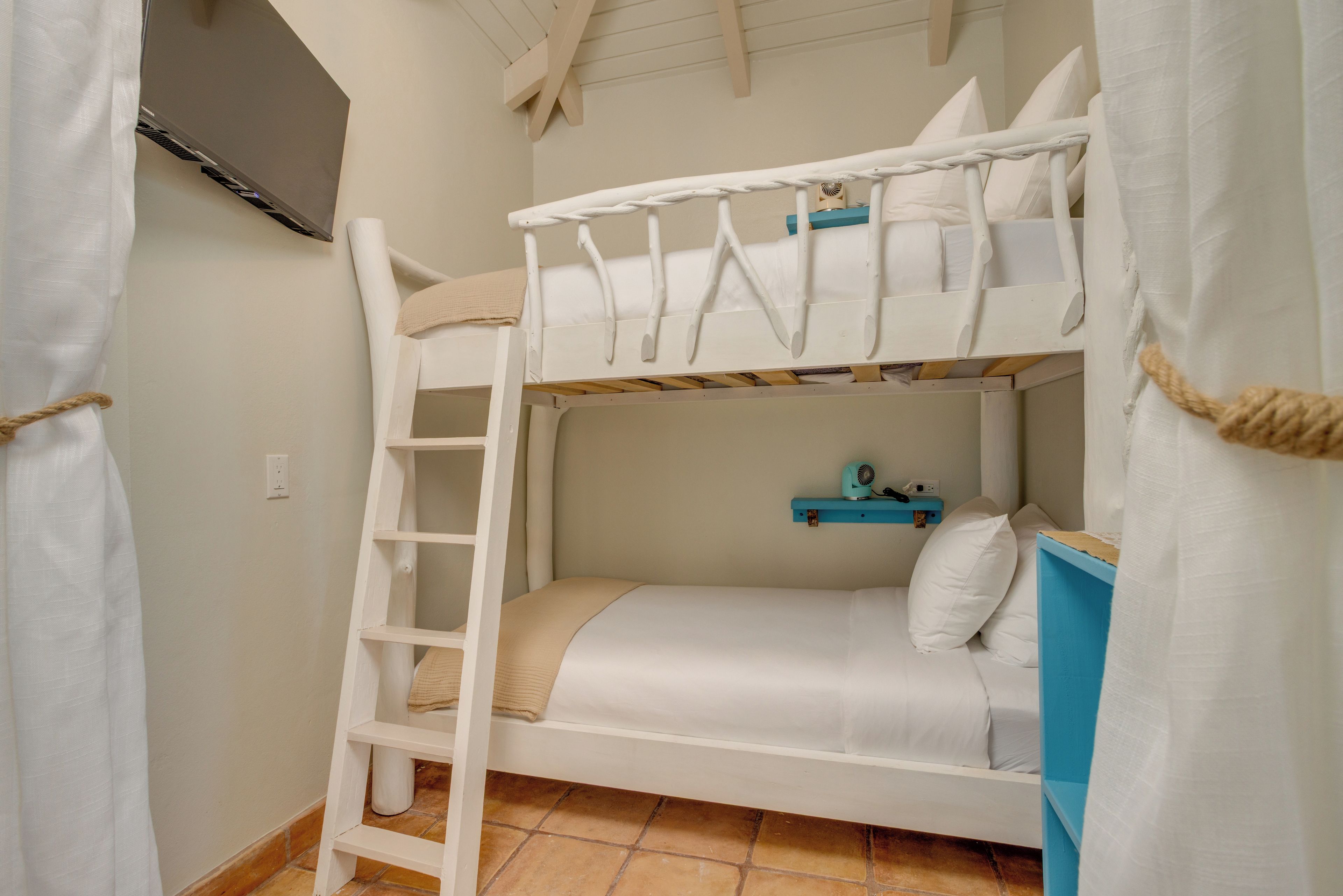 A bunk bed room with a ladder, a shelf with a fan, and a curtain.
