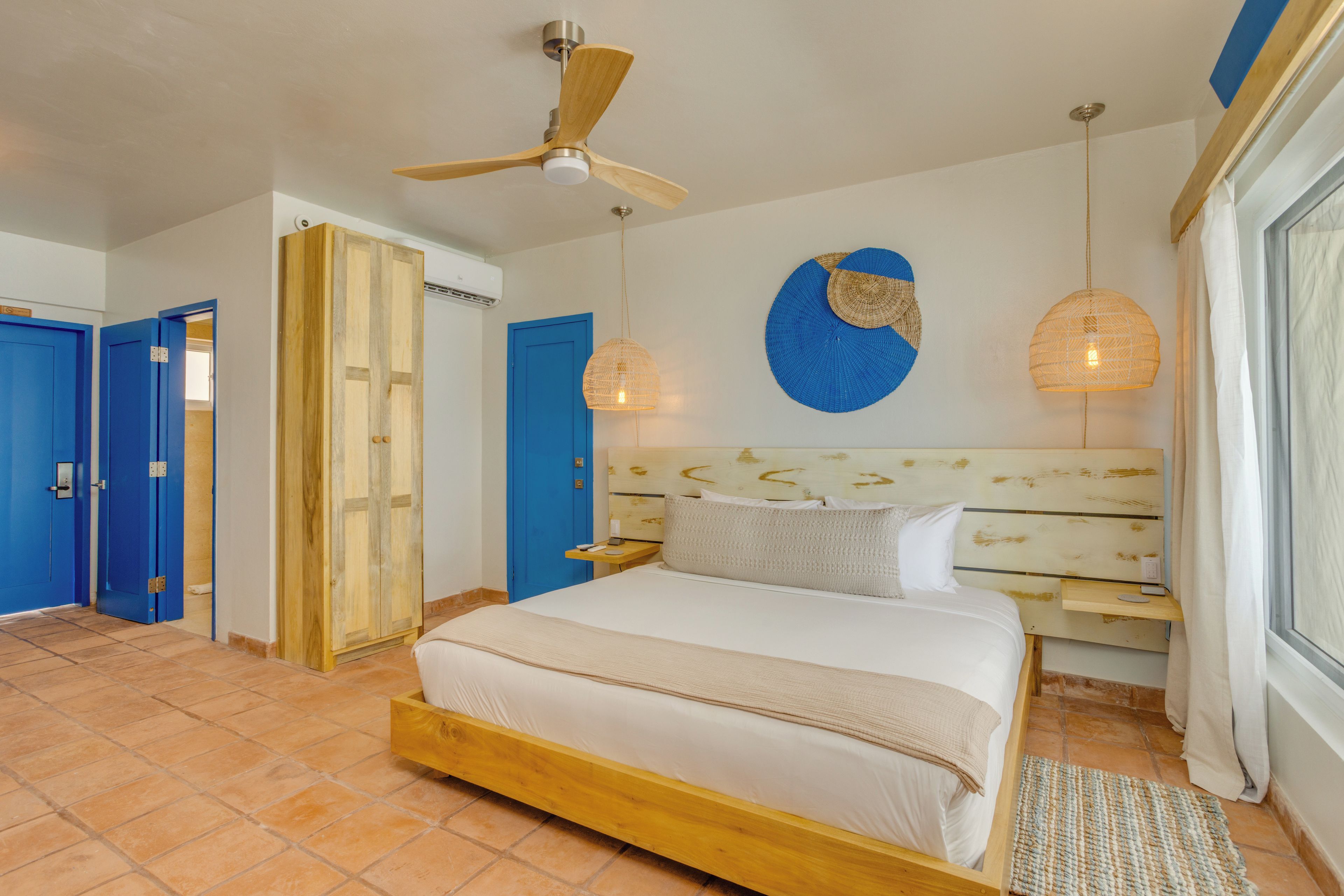 A bedroom with a large bed, a ceiling fan, a blue door, and a wall-mounted light fixture.