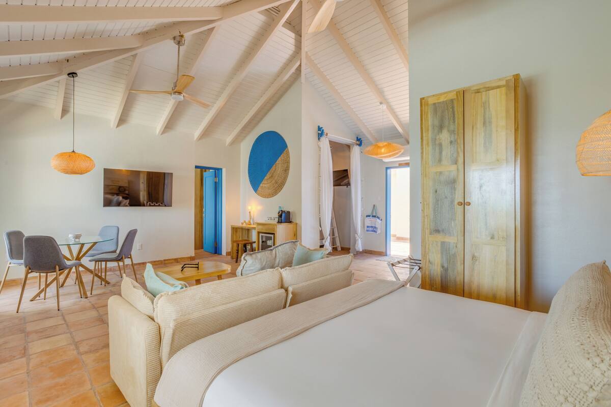 A spacious room with a large bed, a dining area with chairs and a table, and a wooden wardrobe.