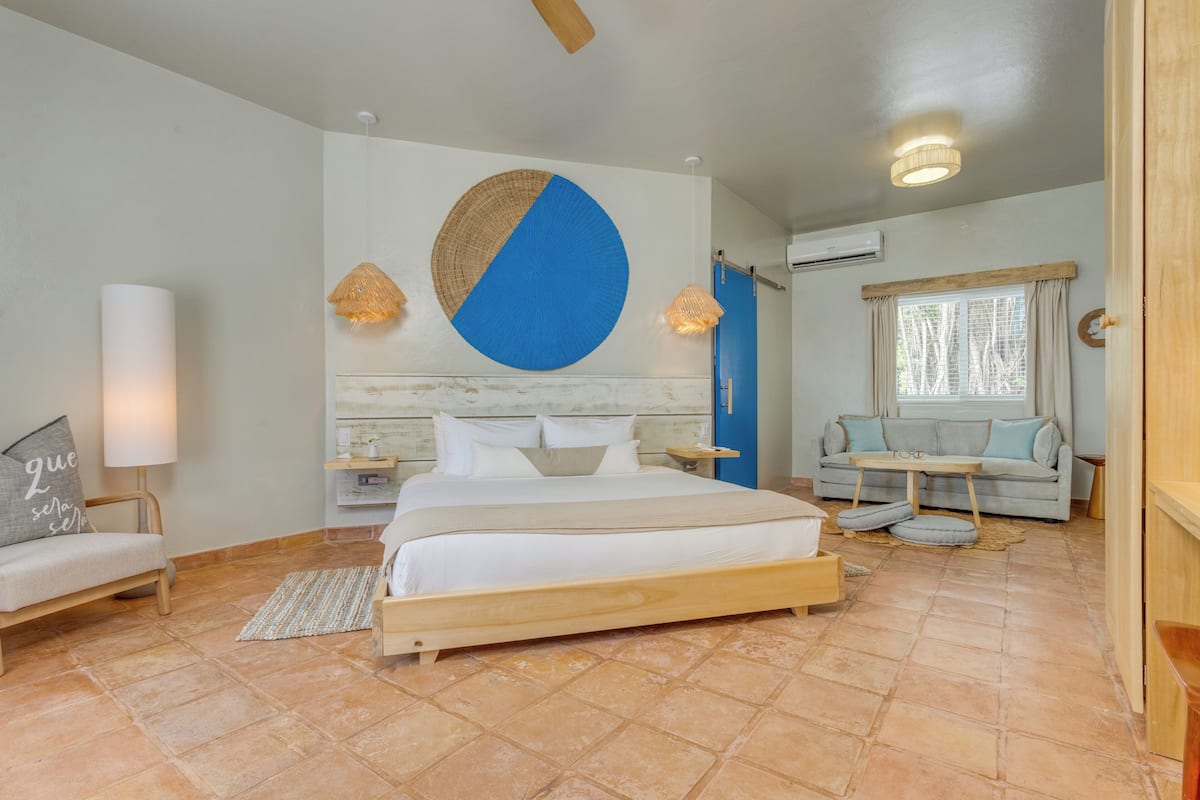 A bedroom with a bed, bedside tables, a sofa, a wall with a circular design, and a window with curtains.