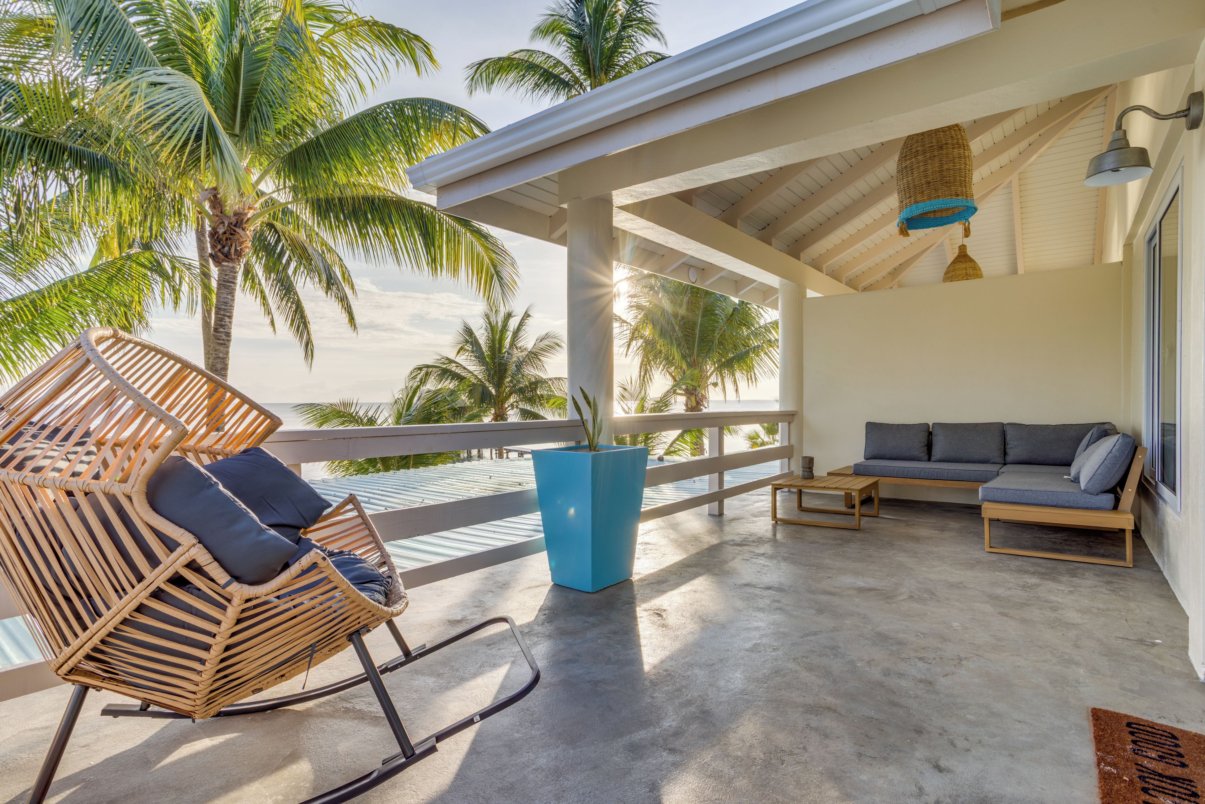 A covered outdoor seating area with a rocking chair, a sofa, and a potted plant.