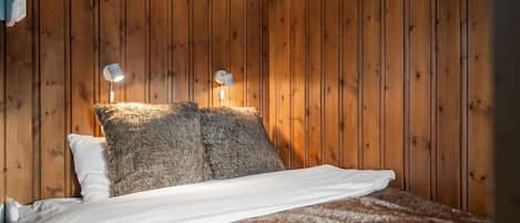 A room with wooden panel walls, a bed with white bedding, and two wall-mounted lamps.