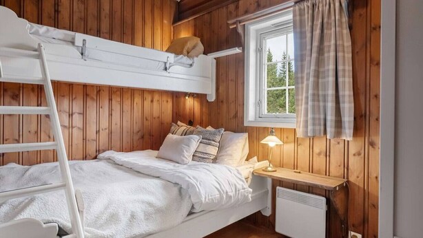 A bunk bed with a ladder, a bedside table with a lamp, a window with curtains, and a radiator. - Trysil Ski-in/out | 6 BR | Sauna (Trysil)