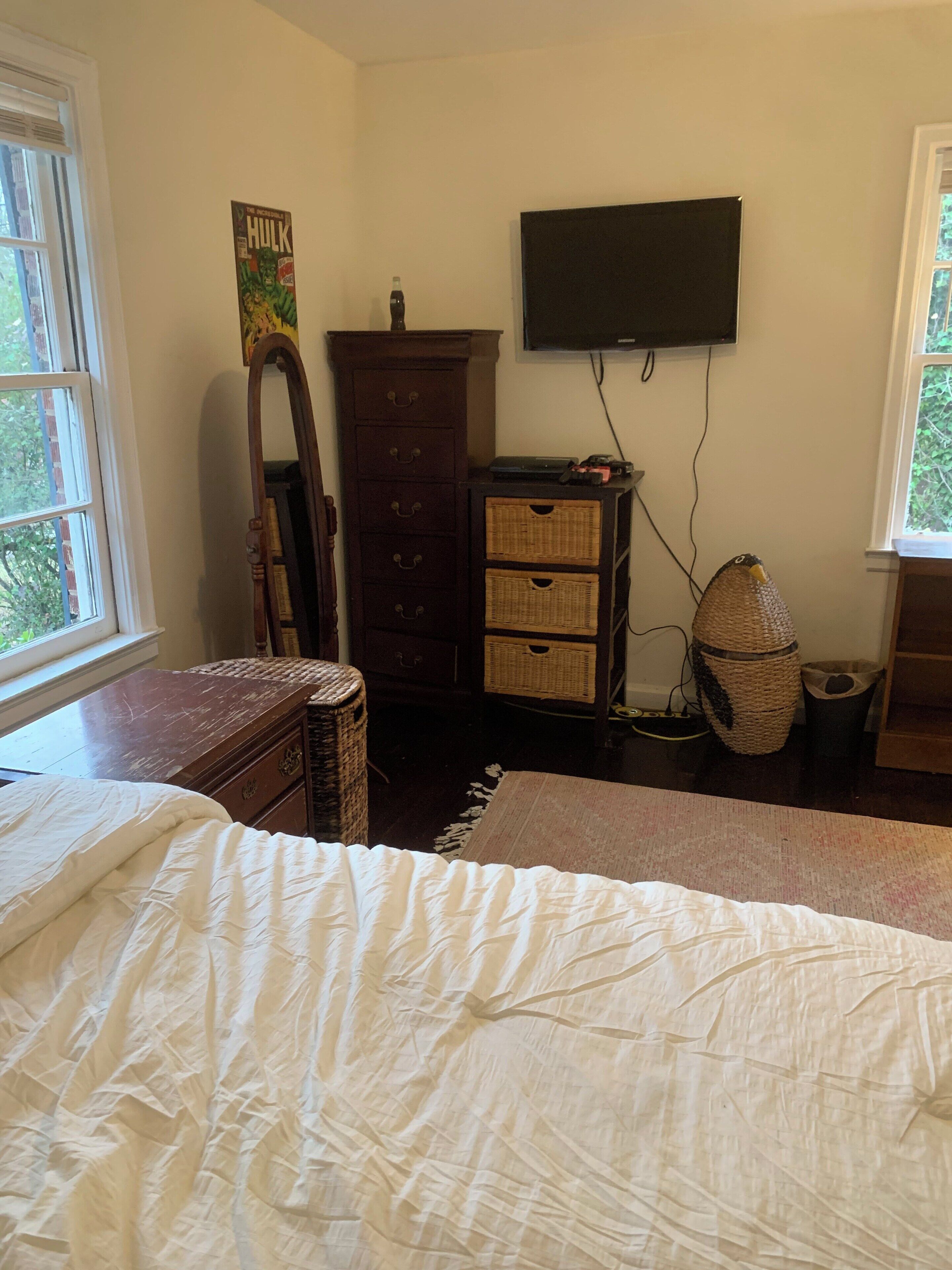 A bedroom with a bed, dresser, television, and a window with a view of trees.