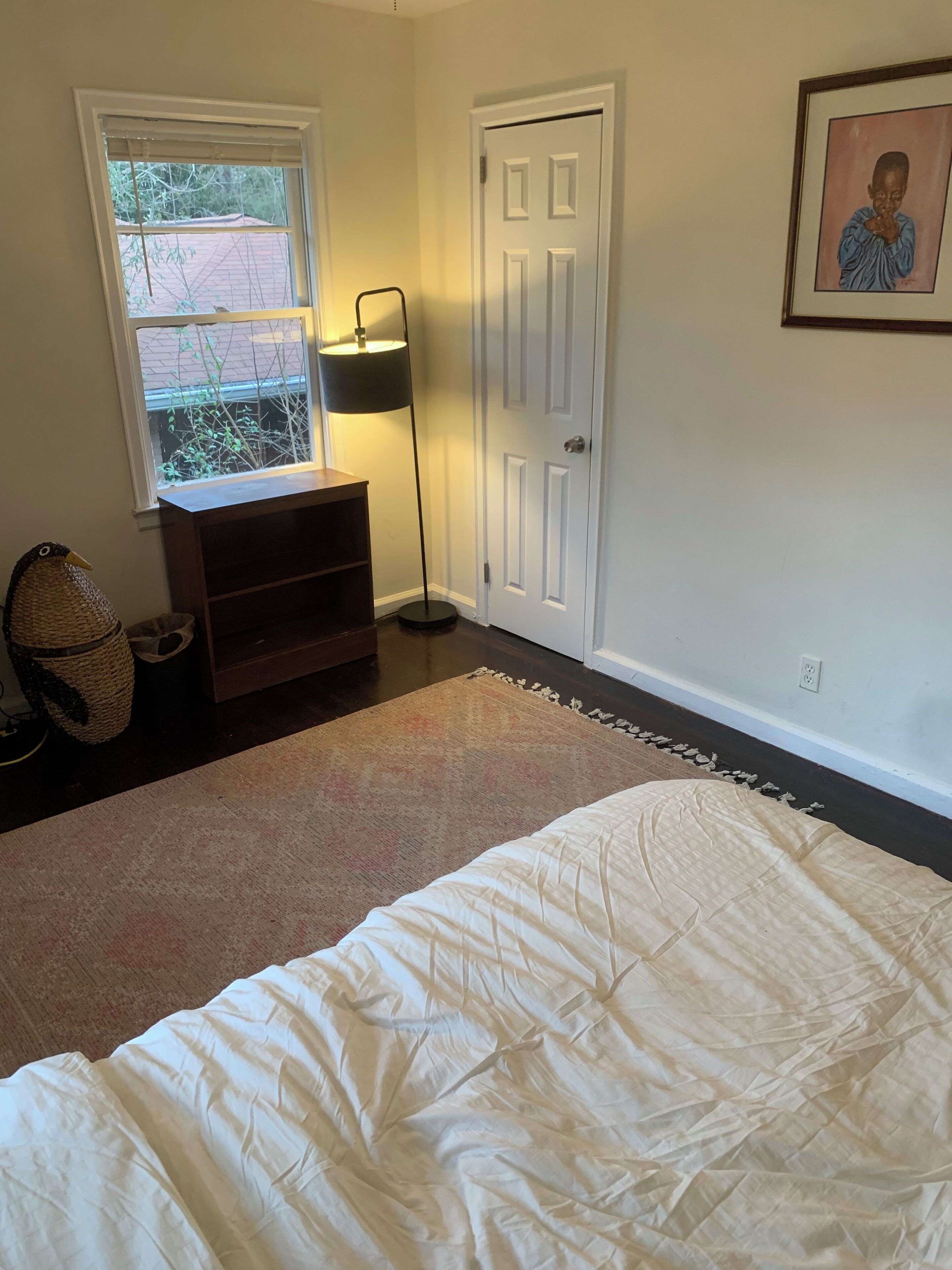 Un dormitorio con cama, mesita de noche, lámpara, puerta y ventana.