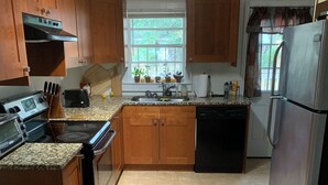 Una cocina con armarios de madera, un refrigerador de acero inoxidable, un lavavajillas y una ventana con plantas.