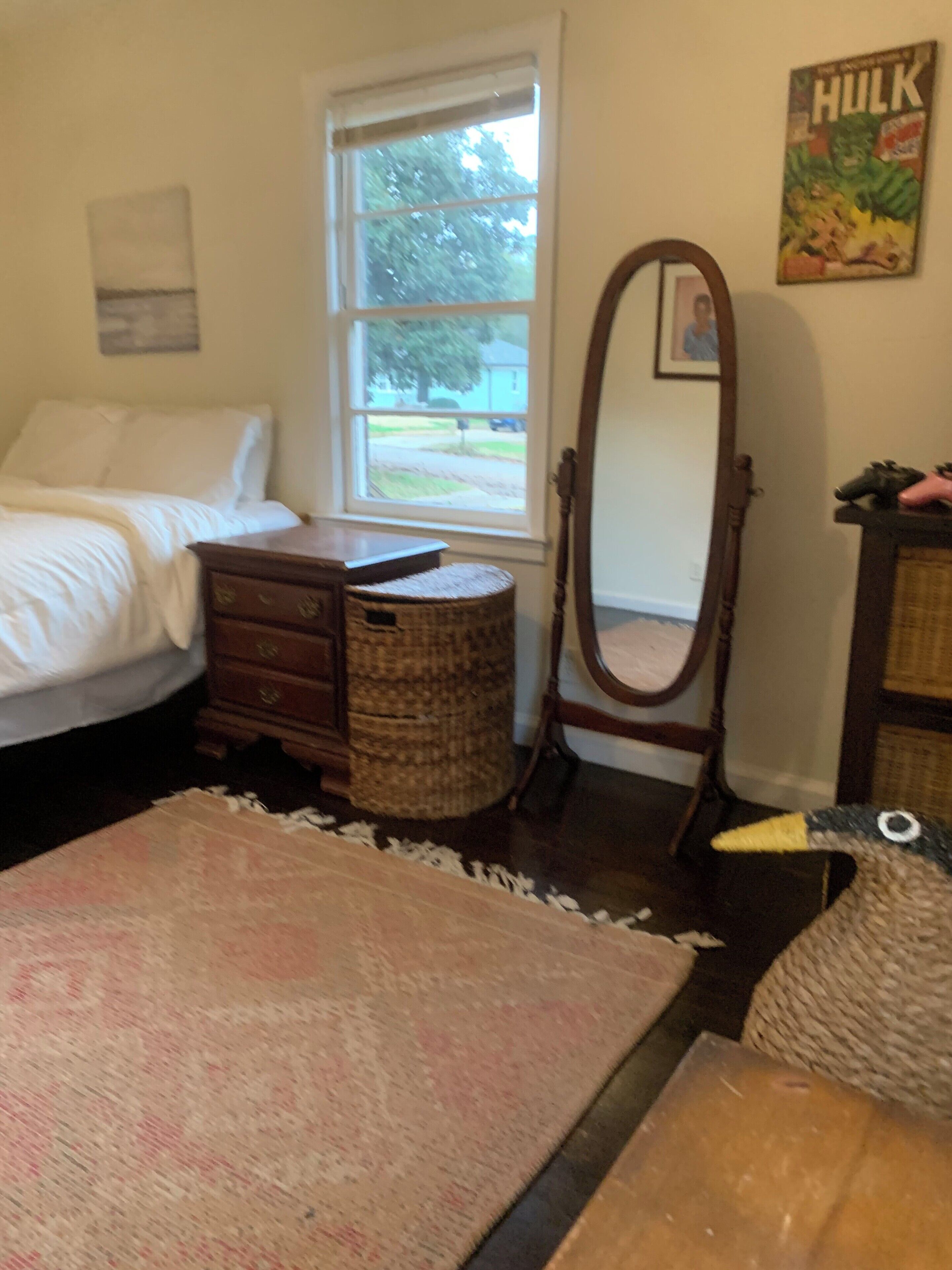 A bedroom with a bed, dresser, mirror, and a window with a view of the outdoors.