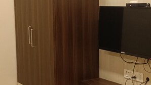 Ein Zimmer mit einem Holzschrank, einem an der Wand befestigten Fernseher und einer Mülleimer.