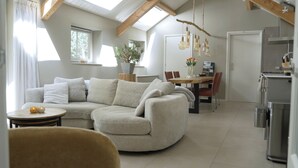 A modern living room with a curved sofa, a dining table with chairs, a kitchen area with a refrigerator, and a skylight. - The William House. Willemstad's best-kept secret. (Willemstad)