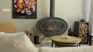 A cozy living room with a wood-burning stove, a round wooden table, a small stool, and a flower painting on the wall. - The William House. Willemstad's best-kept secret. (Willemstad)