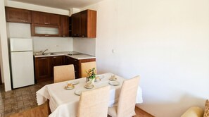A compact kitchen with wooden cabinets, a white refrigerator, and a dining area with a table set for two. - Penthouse Duplex Large 2 Bedroom MP1 (Bansko)
