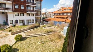 Ein Innenhof mit einem gepflasterten Weg, kleinen Sträuchern und einer Rasenfläche. Im Hintergrund sind mehrstöckige Gebäude mit Balkonen und Fenstern zu sehen.